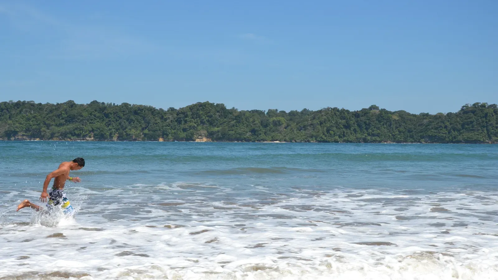 Pengunjung bermain ombak di Pantai Tamban dengan latar bukit hijau