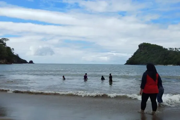 Pantai Wediawu dengan pengunjung berenang dan perbukitan hijau di kedua sisi teluk